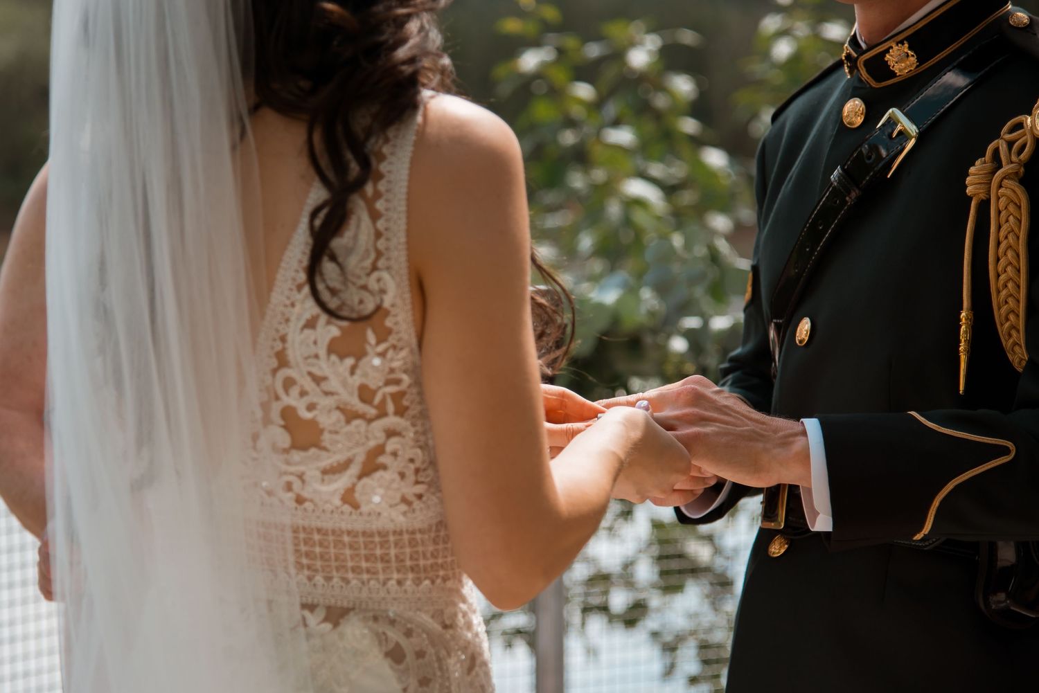 Close up of a white lace wedding dress and military dress uniform during an outdoor wedding ceremony exchange.