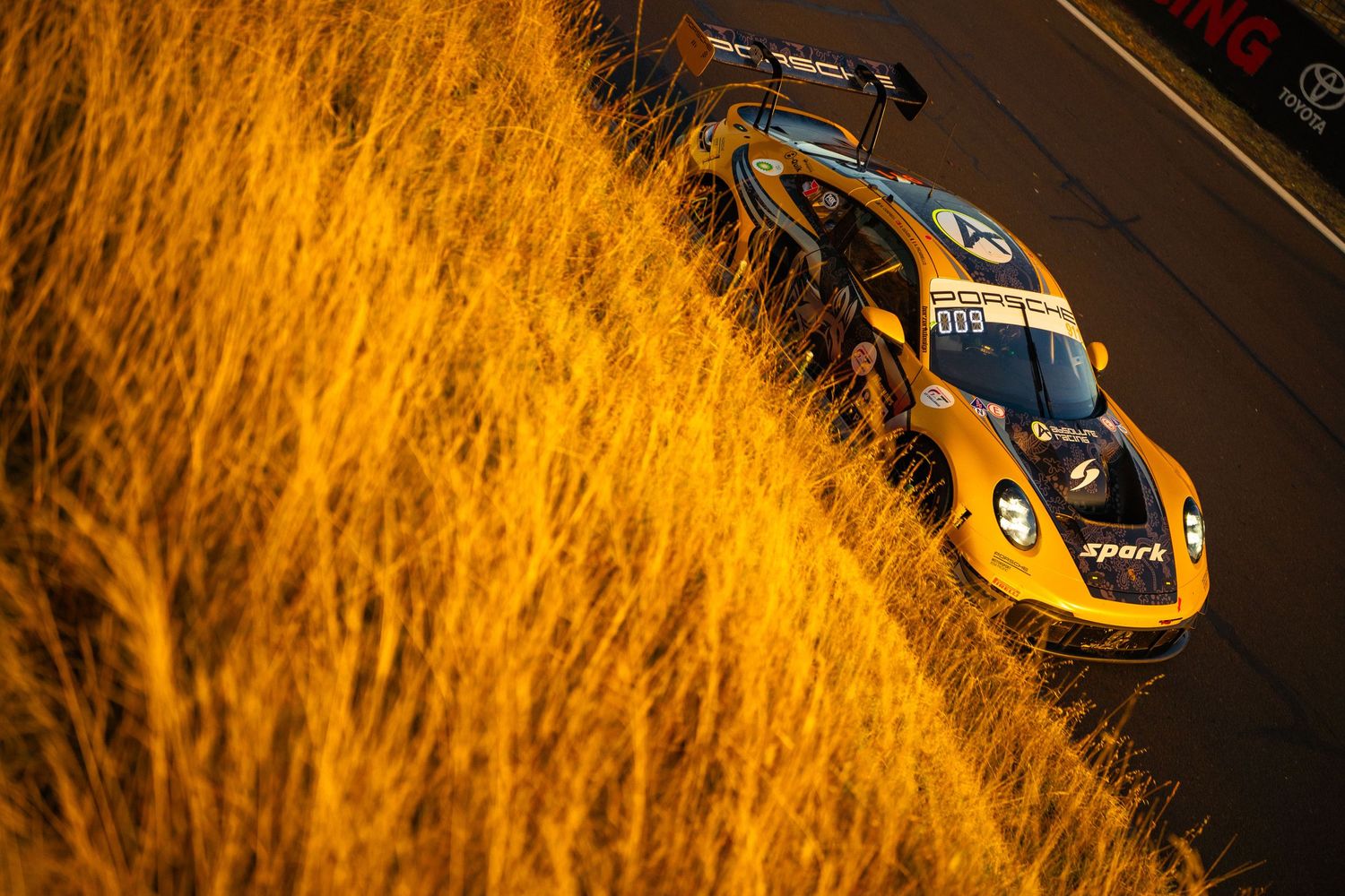 Race car photographed through golden grass during sunset motorsport event.