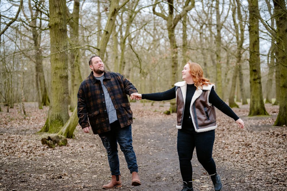 Playful couple having fun and laughing while holding hands on a forest path during an autumn day.