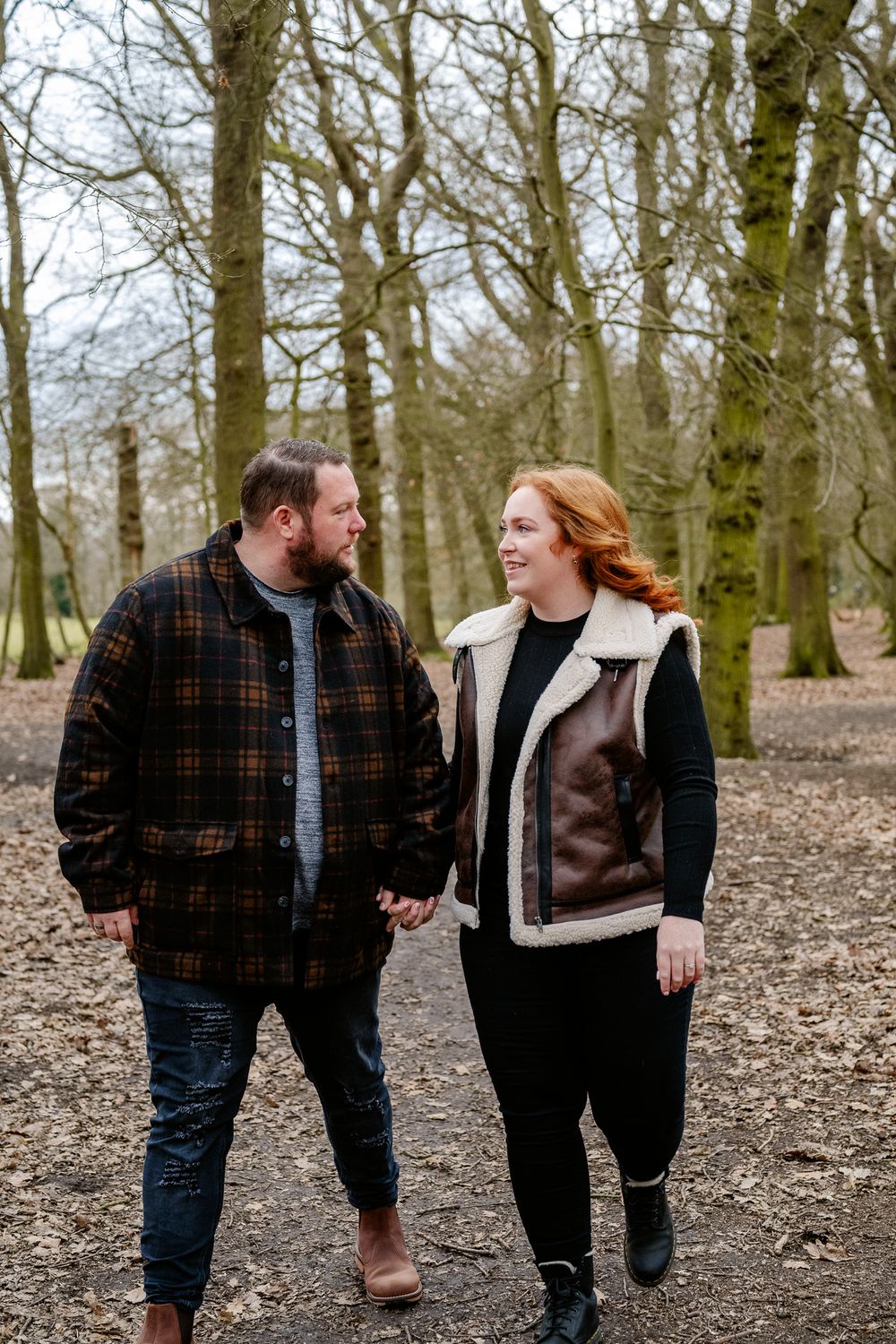 Couple in winter outerwear holding hands while walking through bare winter woods.