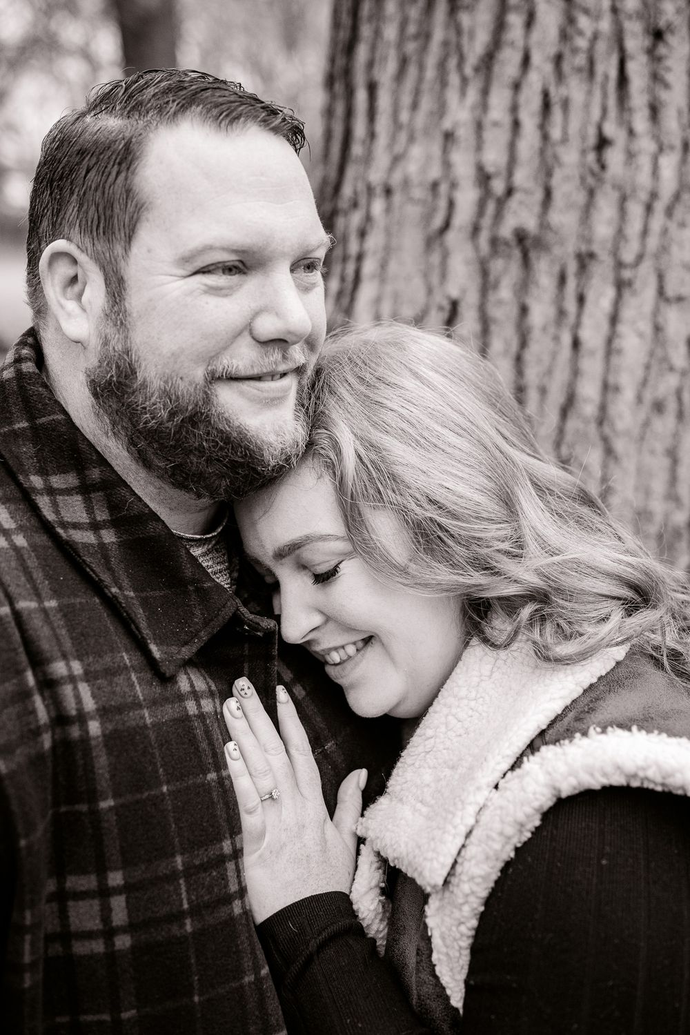 A tender black and white portrait of a couple embracing against a tree trunk background.