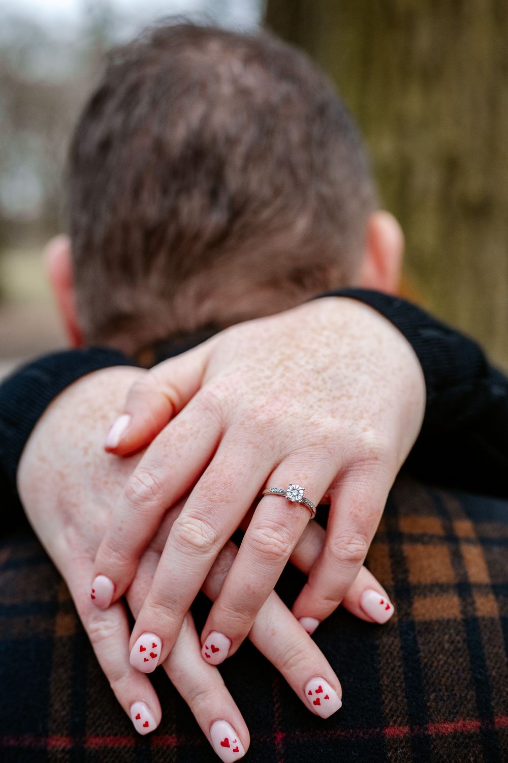 Close-up of hands showing an engagement ring with festive nail art against a plaid jacket.