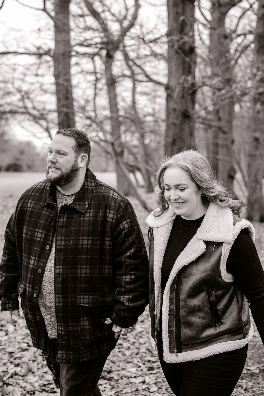 Black and white portrait of couple walking and smiling in winter forest setting.