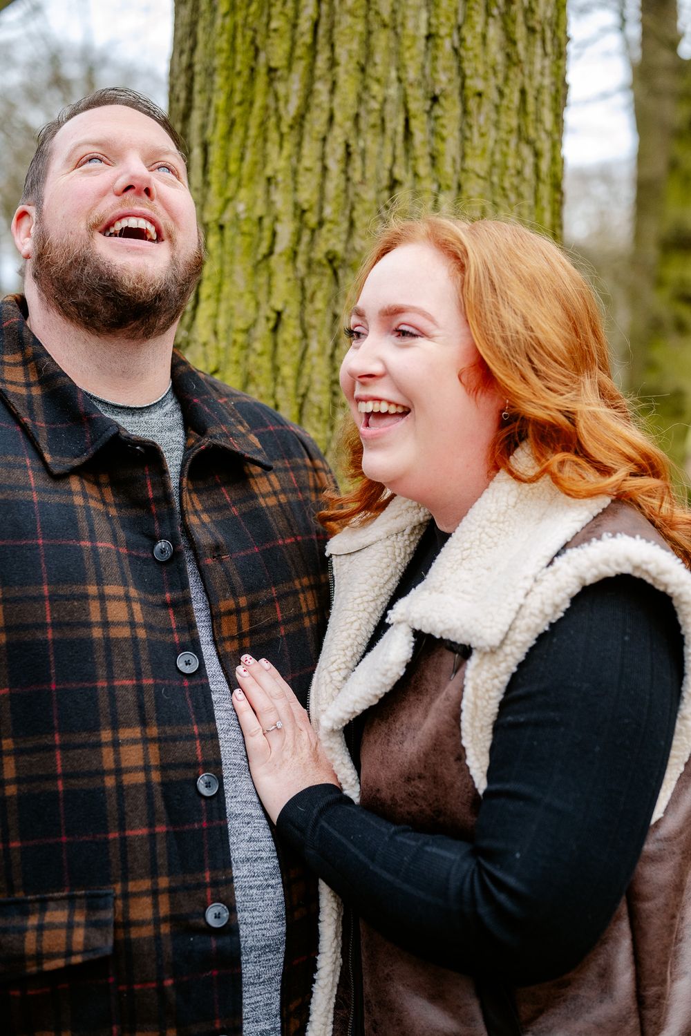 A happy couple sharing a laugh outdoors, wearing matching winter clothing against a forest backdrop.