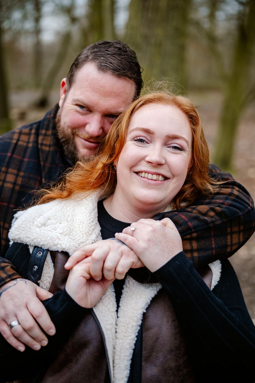 Intimate portrait of couple embracing in casual winter wear among bare trees.