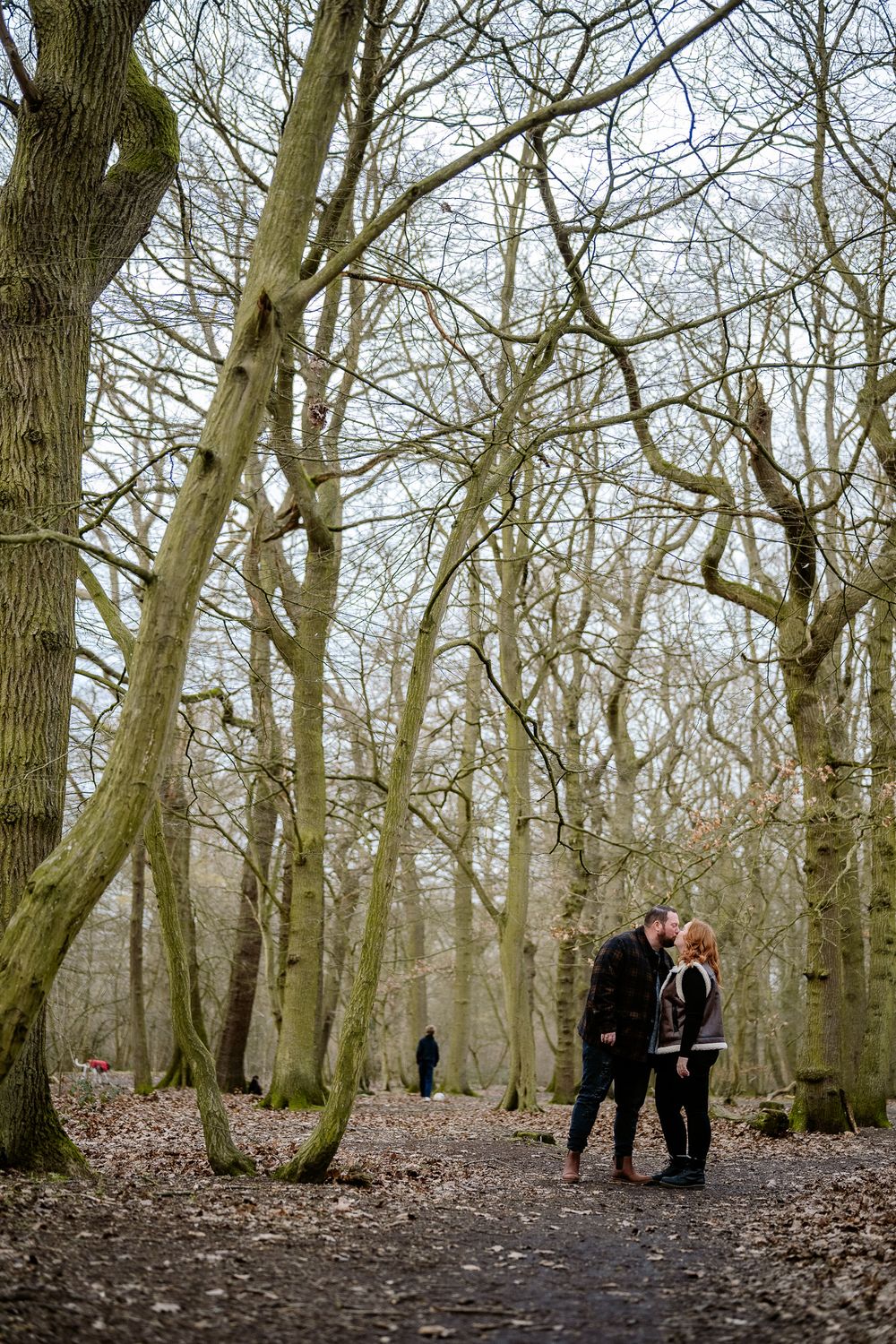 A couple walking together on a leaf-covered path through a winter forest.