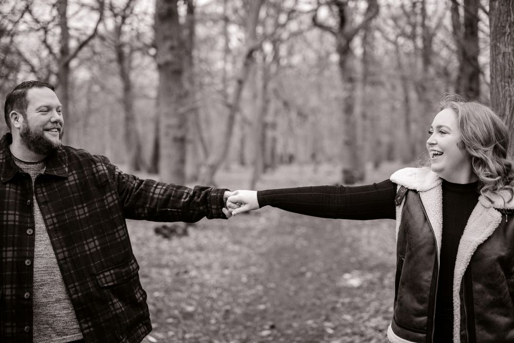 Black and white photo of couple joyfully reaching for each other's hands in a wooded setting.