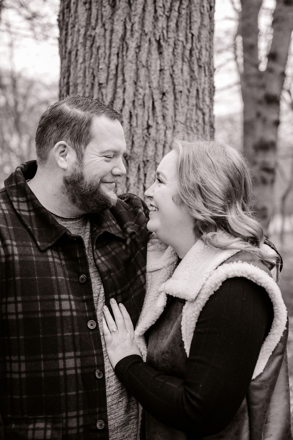 A black and white portrait of a couple laughing together while embracing near a large tree.