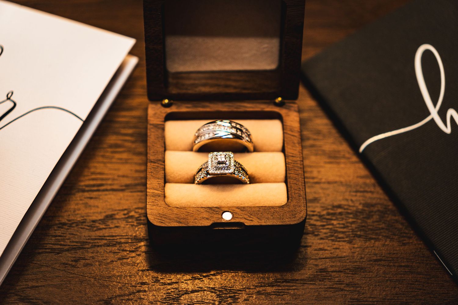 Two wedding bands nestled in a wooden ring box on a dark wooden surface.