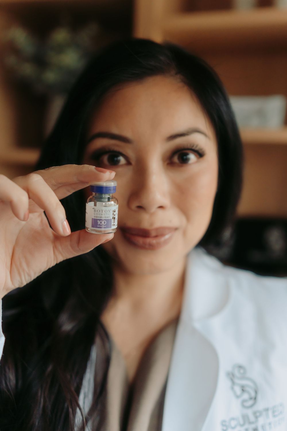 Medical professional in white coat holding up small vaccine vial while demonstrating healthcare product.