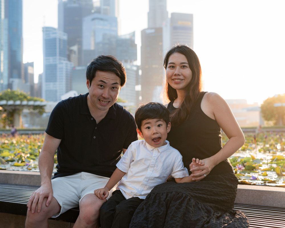Family sitting together on outdoor bench with urban skyline at sunset.