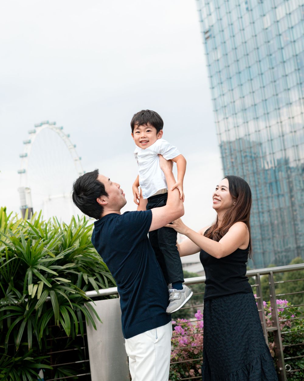 Family playing together in front of Singapore skyline with Marina Bay Sands and Ferris wheel visible.