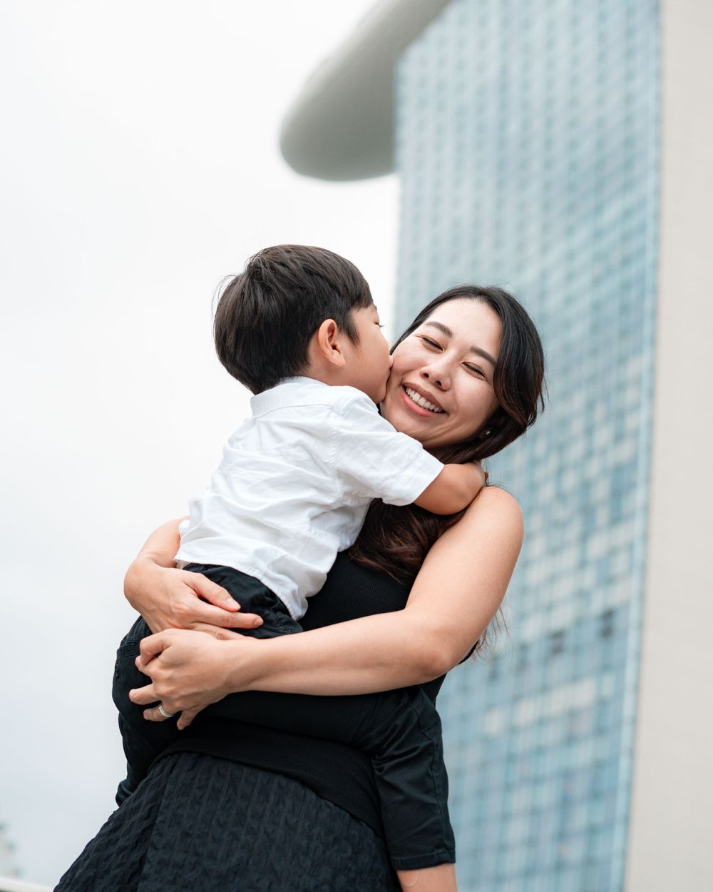 Tender embrace shared between parent and child against modern city architecture.