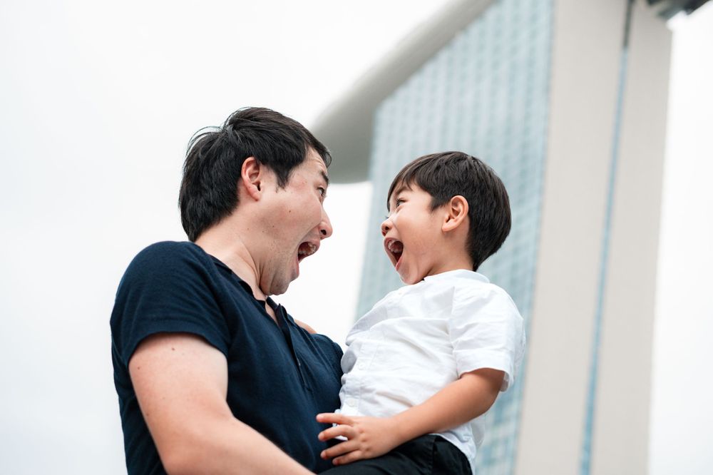Candid moment of shared laughter between parent and child against urban backdrop.