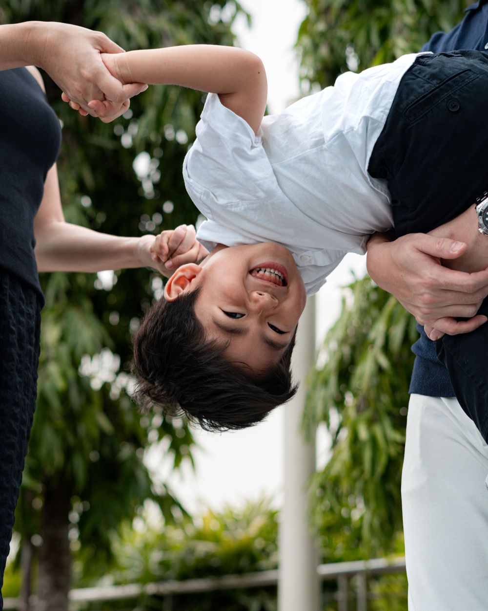 Carefree family playtime with child held upside down outdoors.
