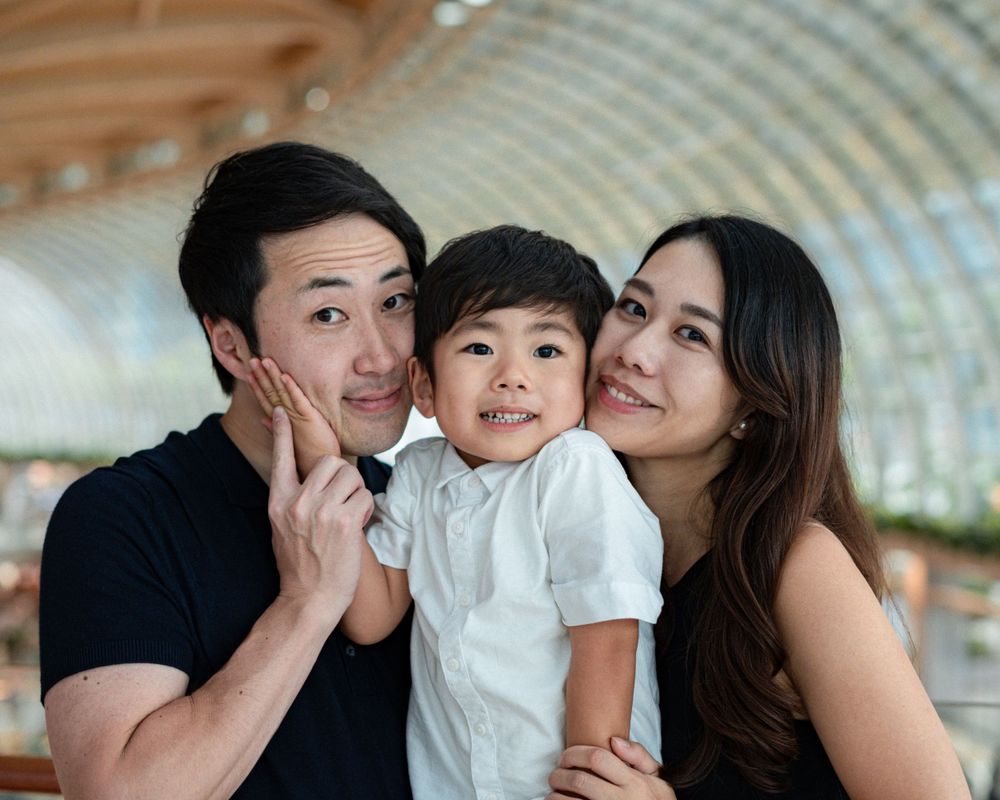 Family portrait taken inside modern shopping center with curved glass ceiling.