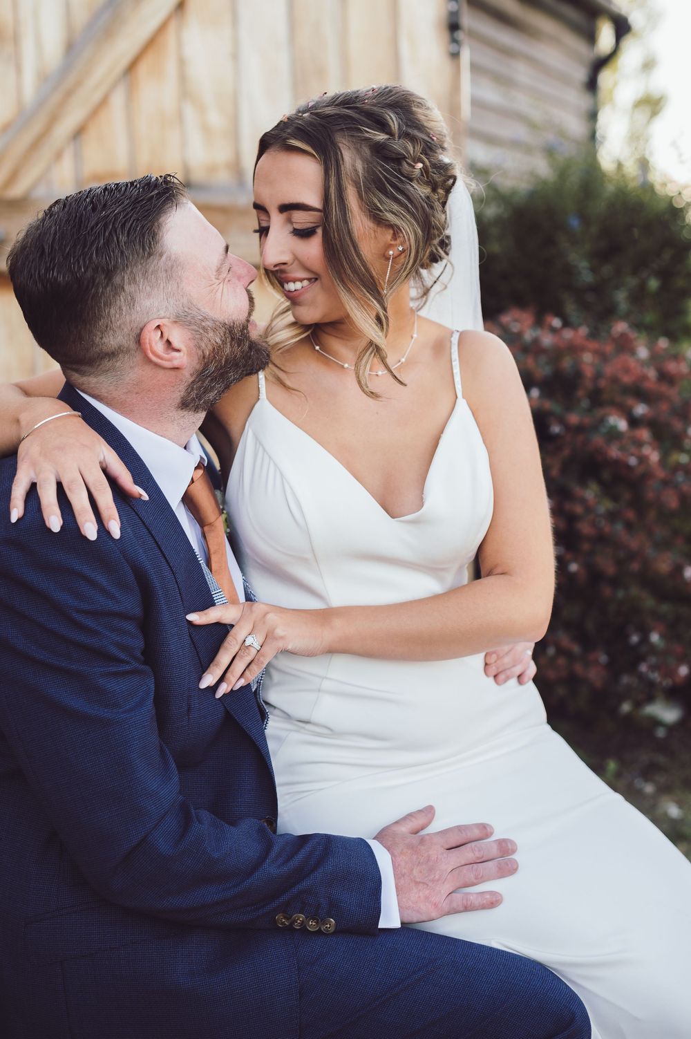 Newlyweds share intimate moments outdoors, with bride in white dress and groom in navy suit.