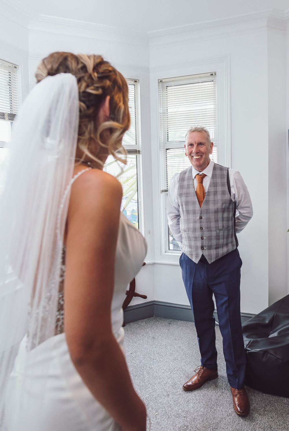 A heartwarming first look moment between a father in a grey vest and his daughter in a wedding dress.