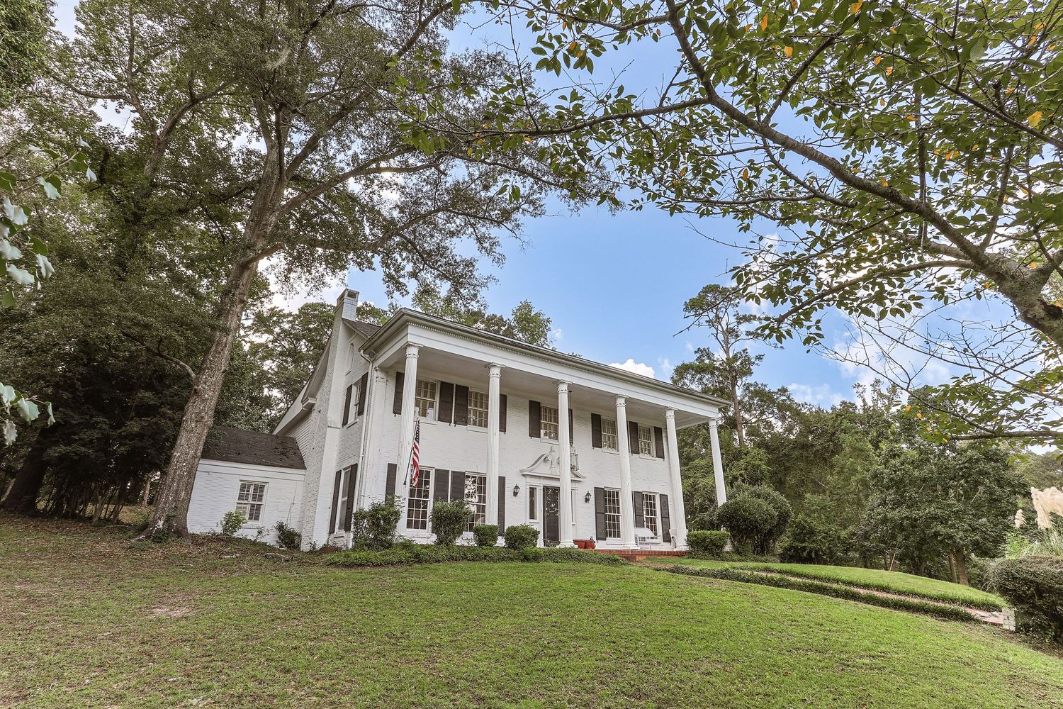 Curved concrete driveway leading to a modern ranch house with manicured lawn and tall pine trees in background.