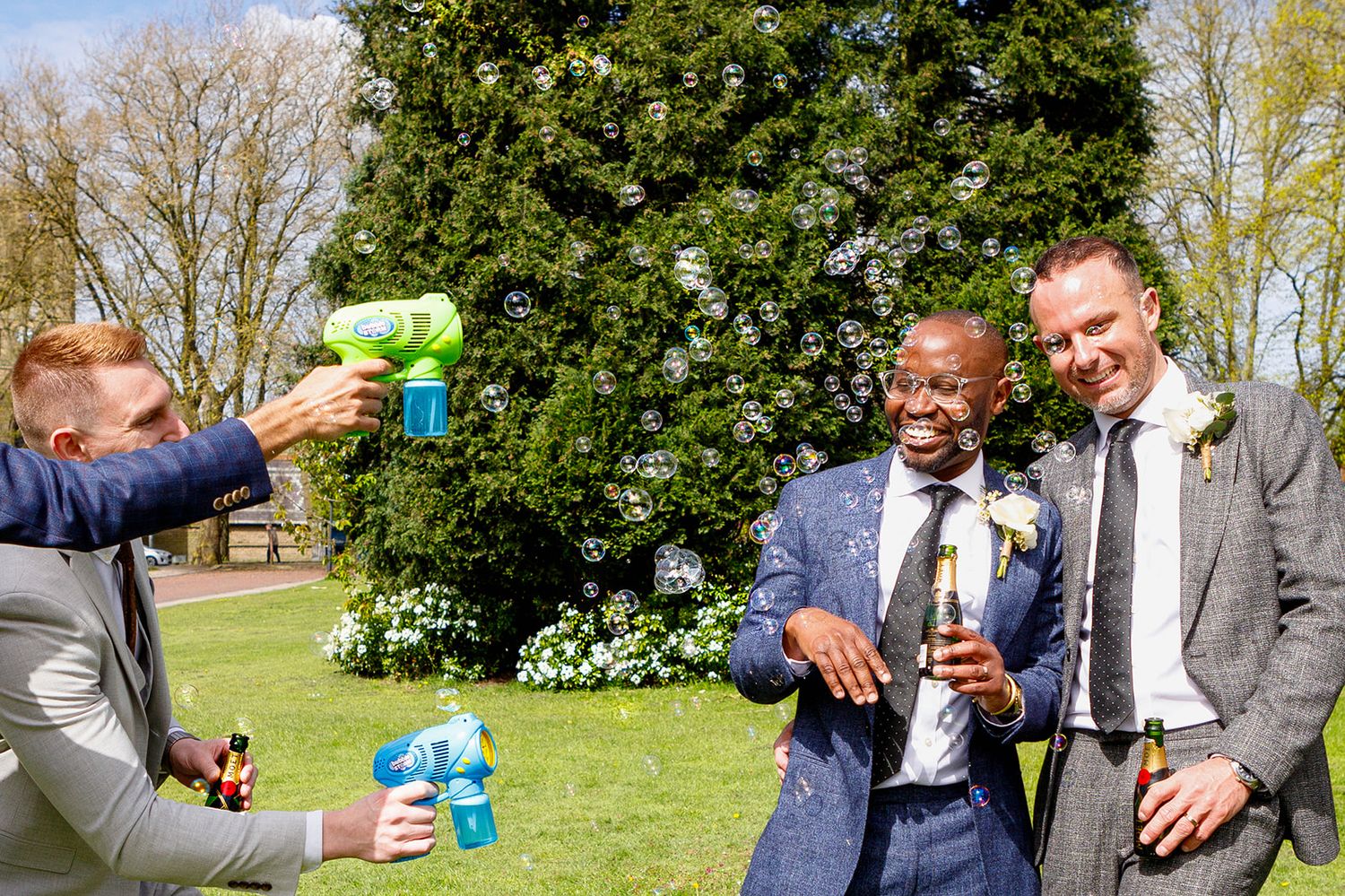 People celebrating outdoors with drinks in a garden setting with blooming shrubs and trees in the background.