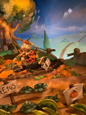 A whimsical garden scene with vegetables, garden markers, and a playful character riding a tractor through the plants.