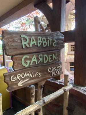 Rustic wooden directional signs point to different areas like 'Grownups', 'Kids', 'Rabbits', and 'Garden' in an outdoor setting.