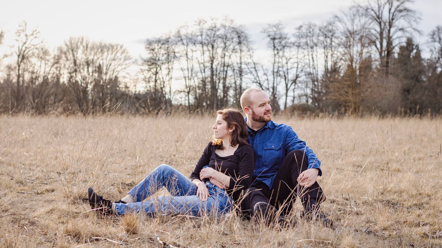 a man and woman sit together in a vast, golden field and look opposite directions