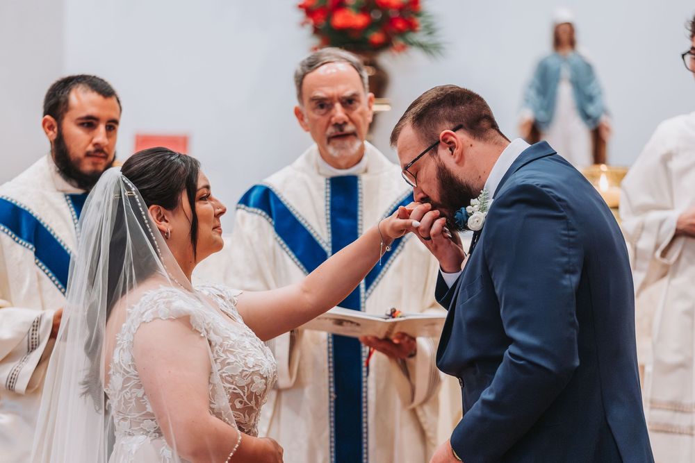 A couple participates in their wedding ceremony with clergy members in white robes inside a church during an emotional moment.