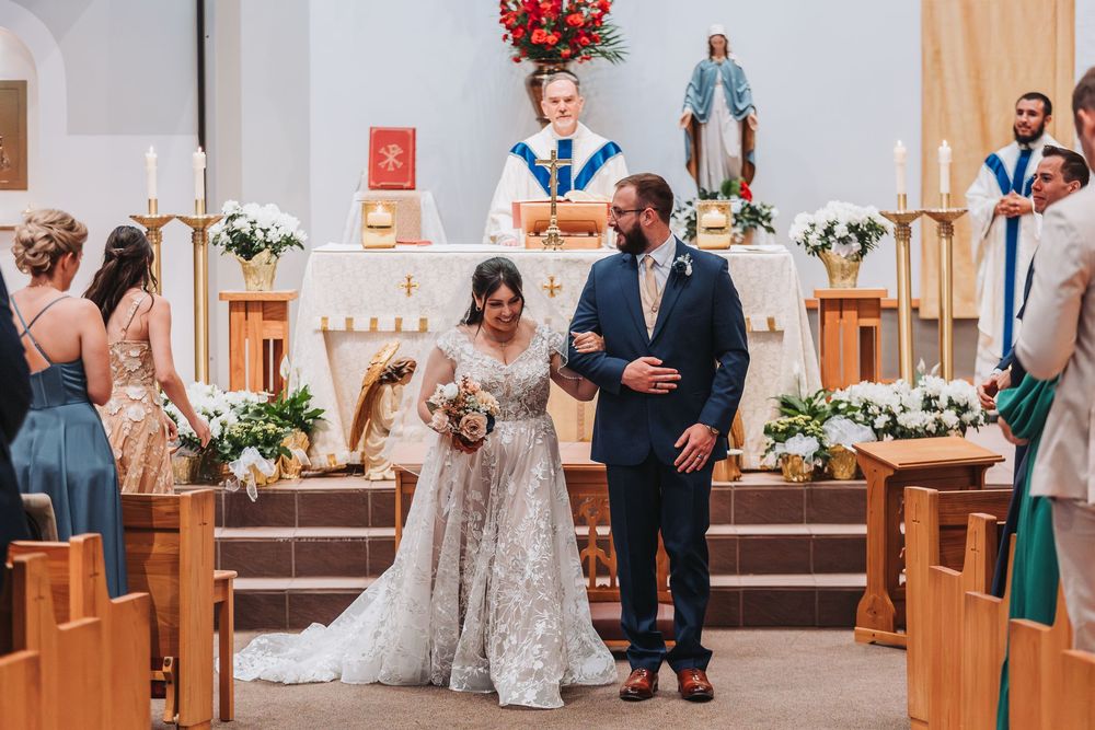 A couple celebrates their wedding ceremony in a Catholic church decorated with white floral arrangements.