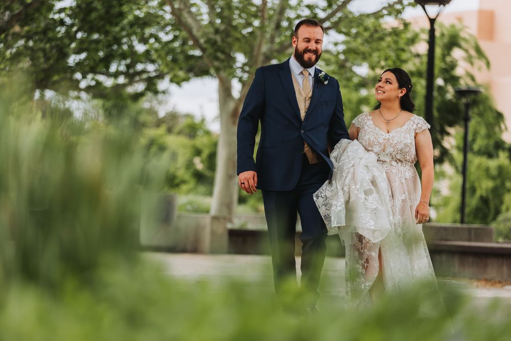 A couple in elegant wedding attire walks together through a lush garden setting during their outdoor celebration.