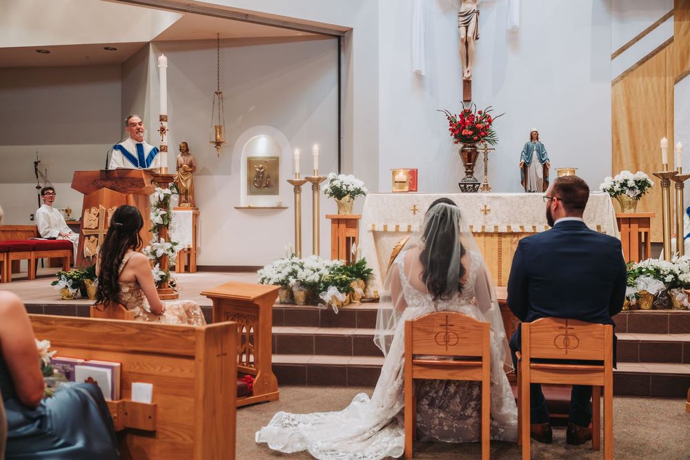 Catholic wedding ceremony underway in a church sanctuary with wooden pews and floral decorations.