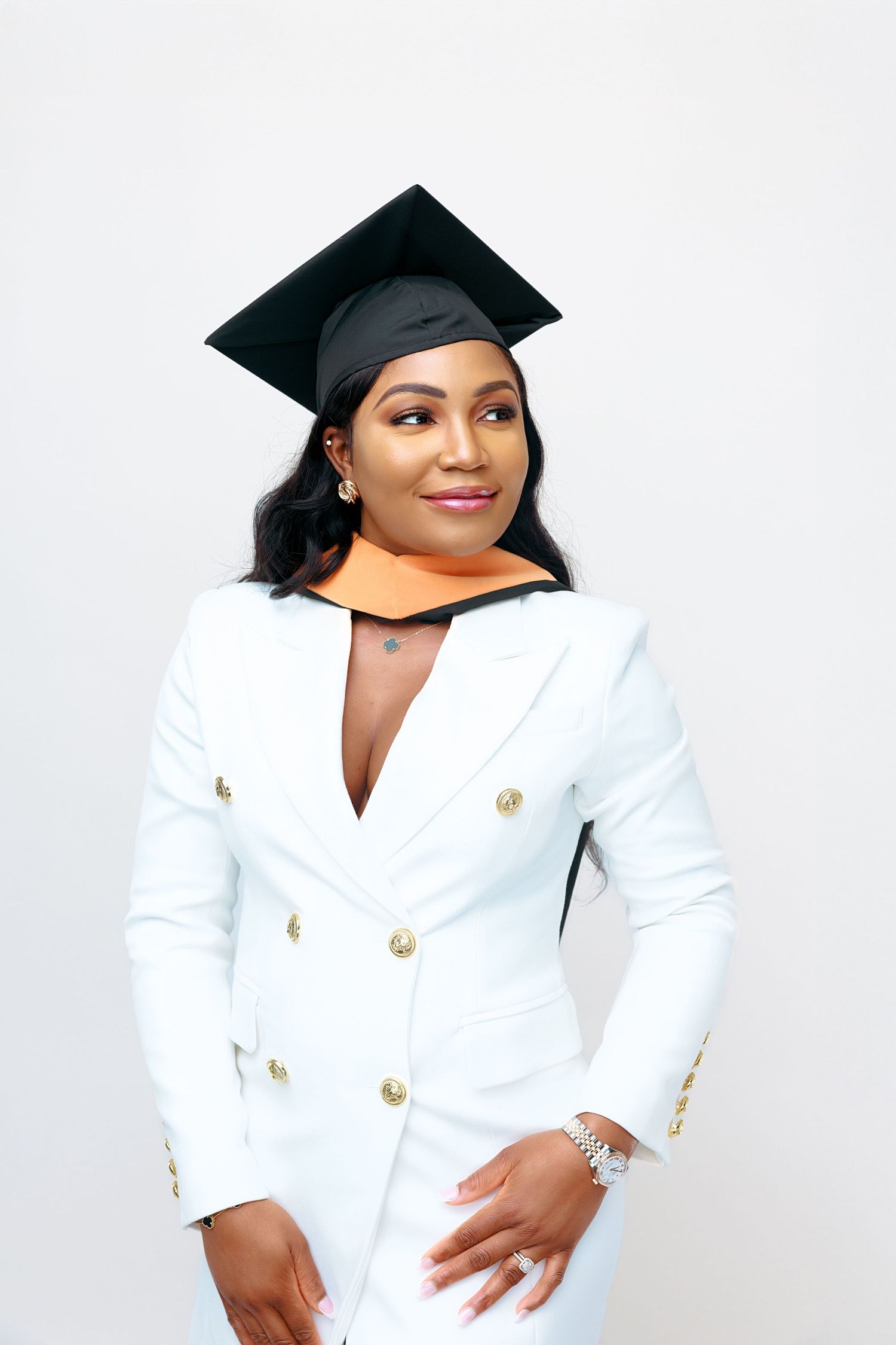 Graduate in white blazer and black cap posing for a portrait against white background.