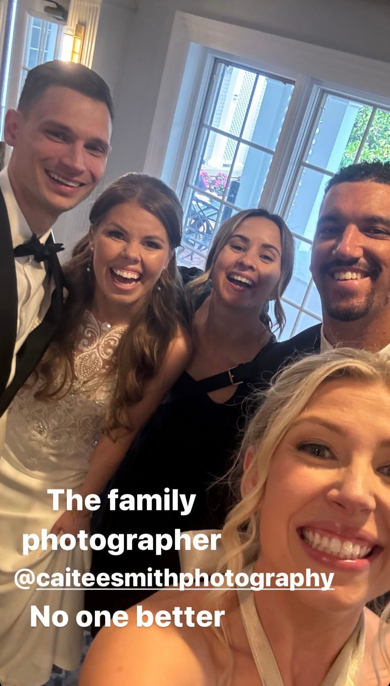 Group of people taking selfies together indoors showing joyful expressions in front of windows.