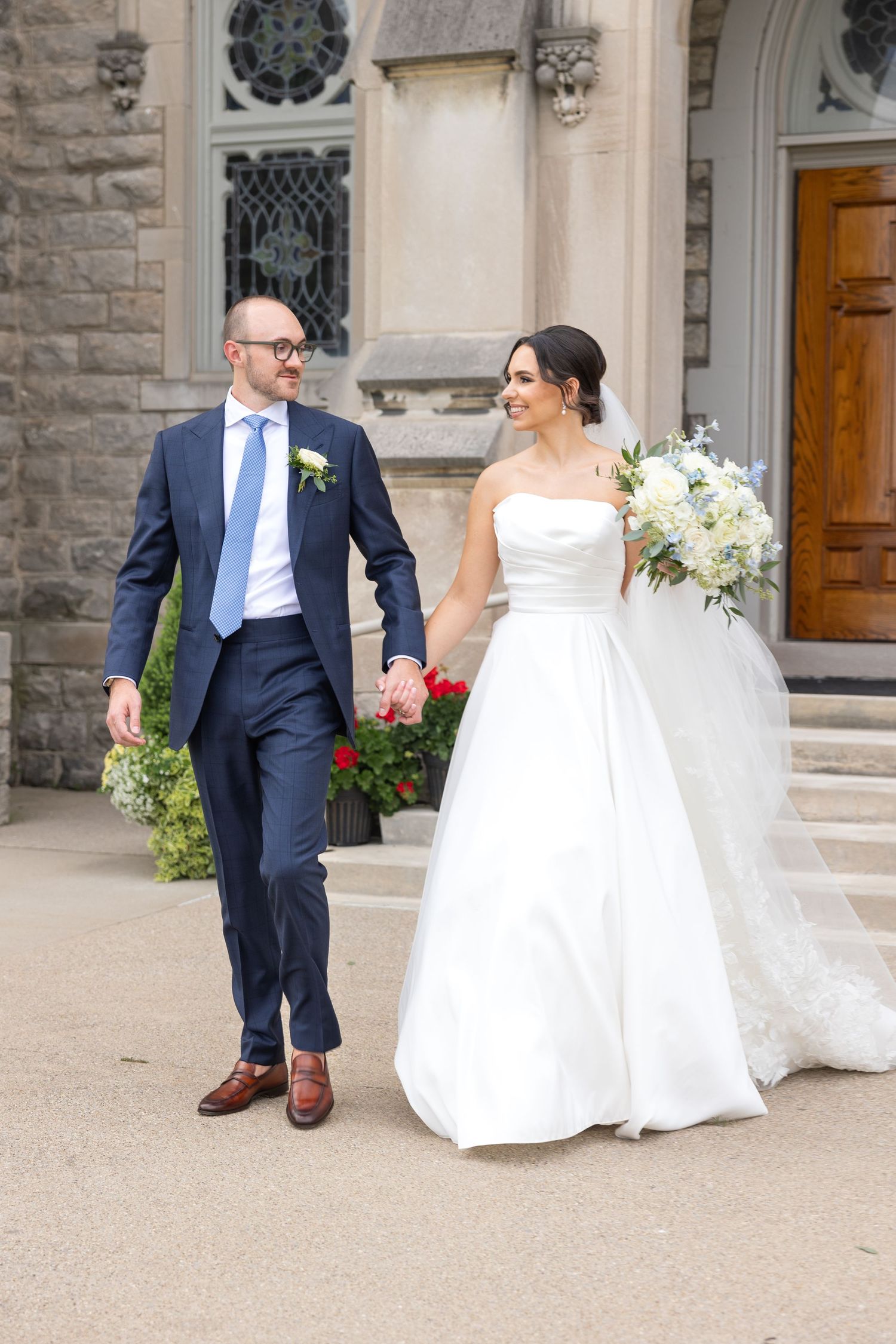 A wedding couple sits together outside a stone church building with ornate architectural details. Rachel Martinez Photography Metro Detroit