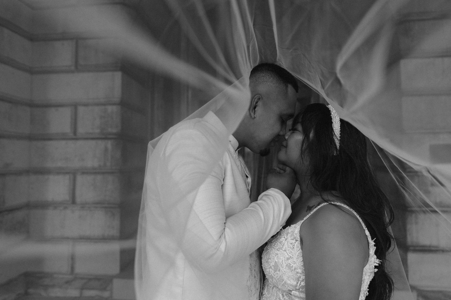 Black and white wedding photo with couple embracing under flowing veil.