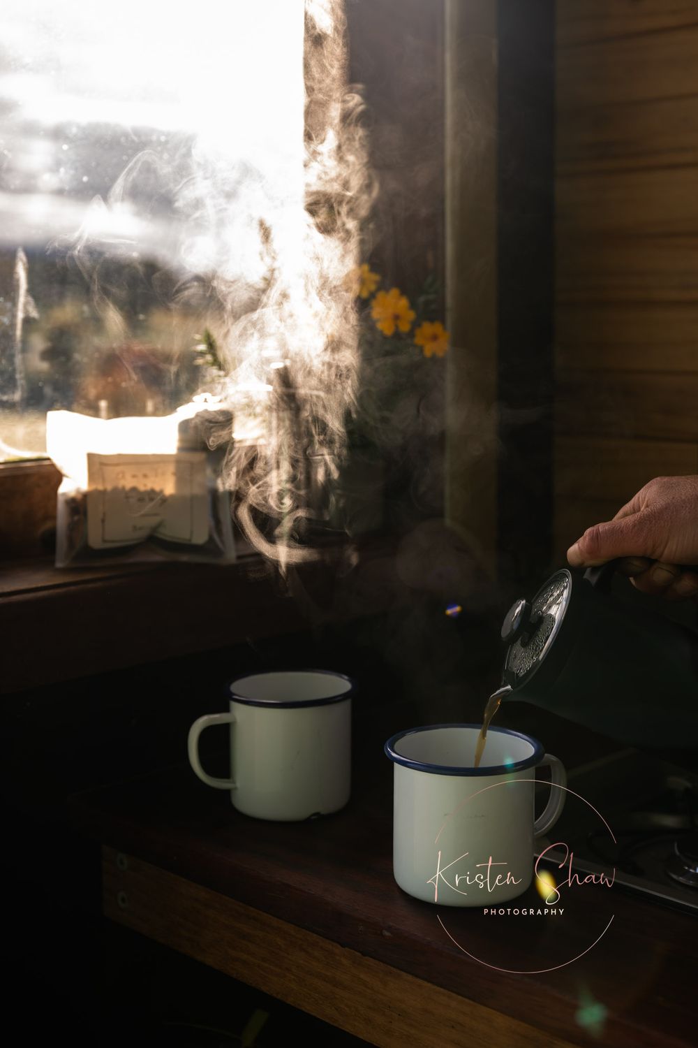 Steam rises from white enamel mugs on a wooden surface with soft morning light streaming through the window.