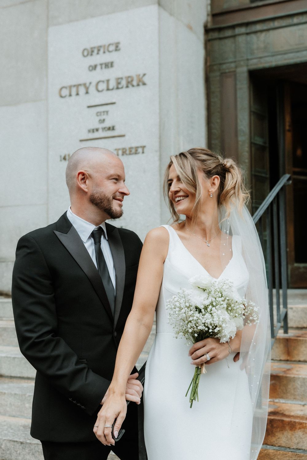 A bride and groom share intimate moments outside a city clerk's office in a series of candid wedding photos.
