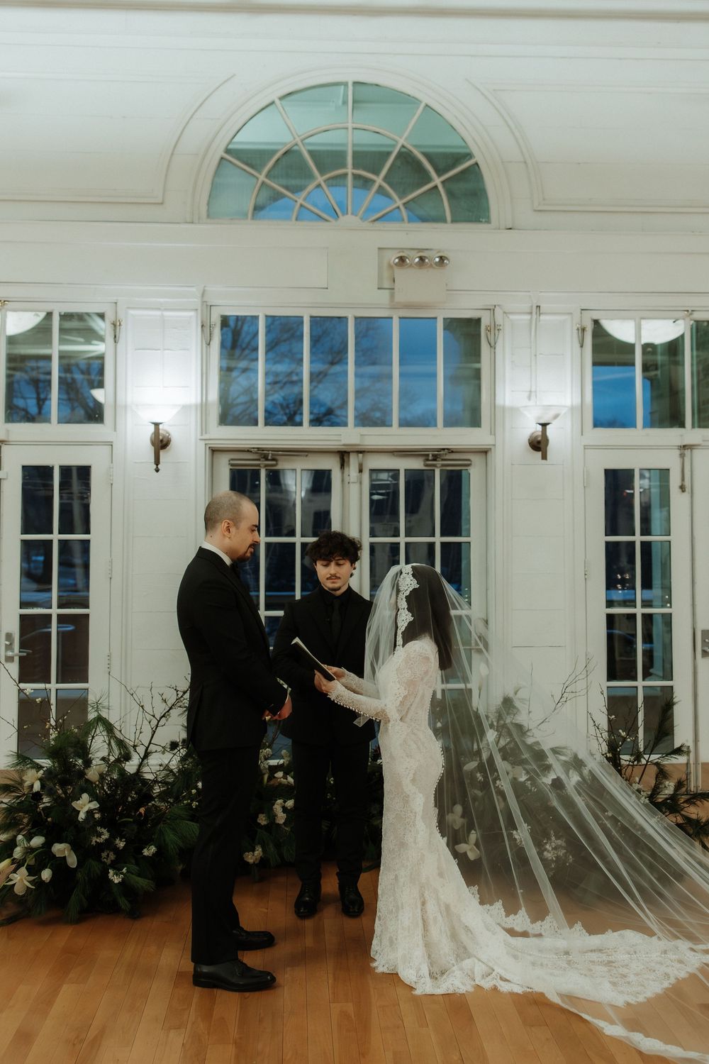 A series of wedding ceremony photos showing a first look moment in an elegant room with large arched windows and hardwood floors.