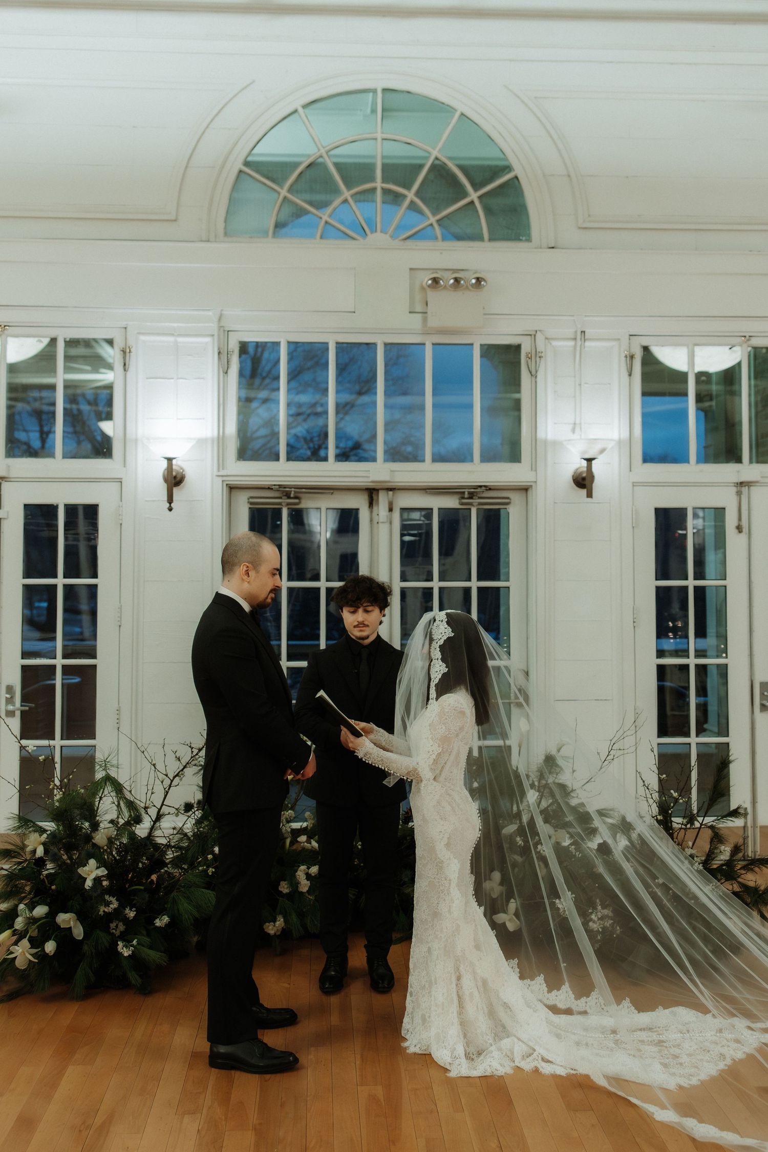 A series of wedding ceremony photos showing a first look moment in an elegant room with large arched windows and hardwood floors.