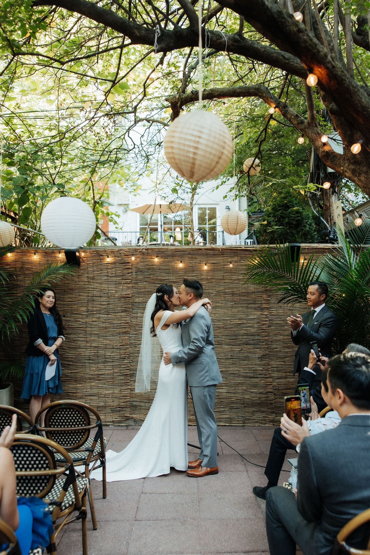 Romantic outdoor wedding ceremony in a garden setting with string lights and paper lanterns creating an intimate atmosphere.