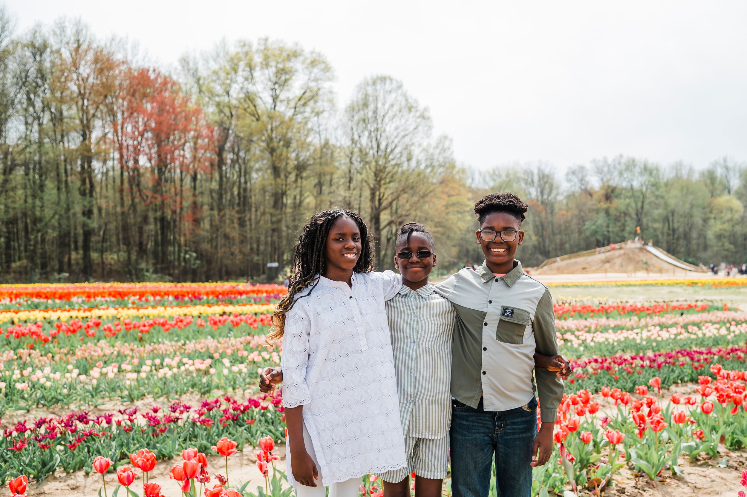 Group standing together in a vibrant tulip field with colorful flowers and autumn trees in the background.