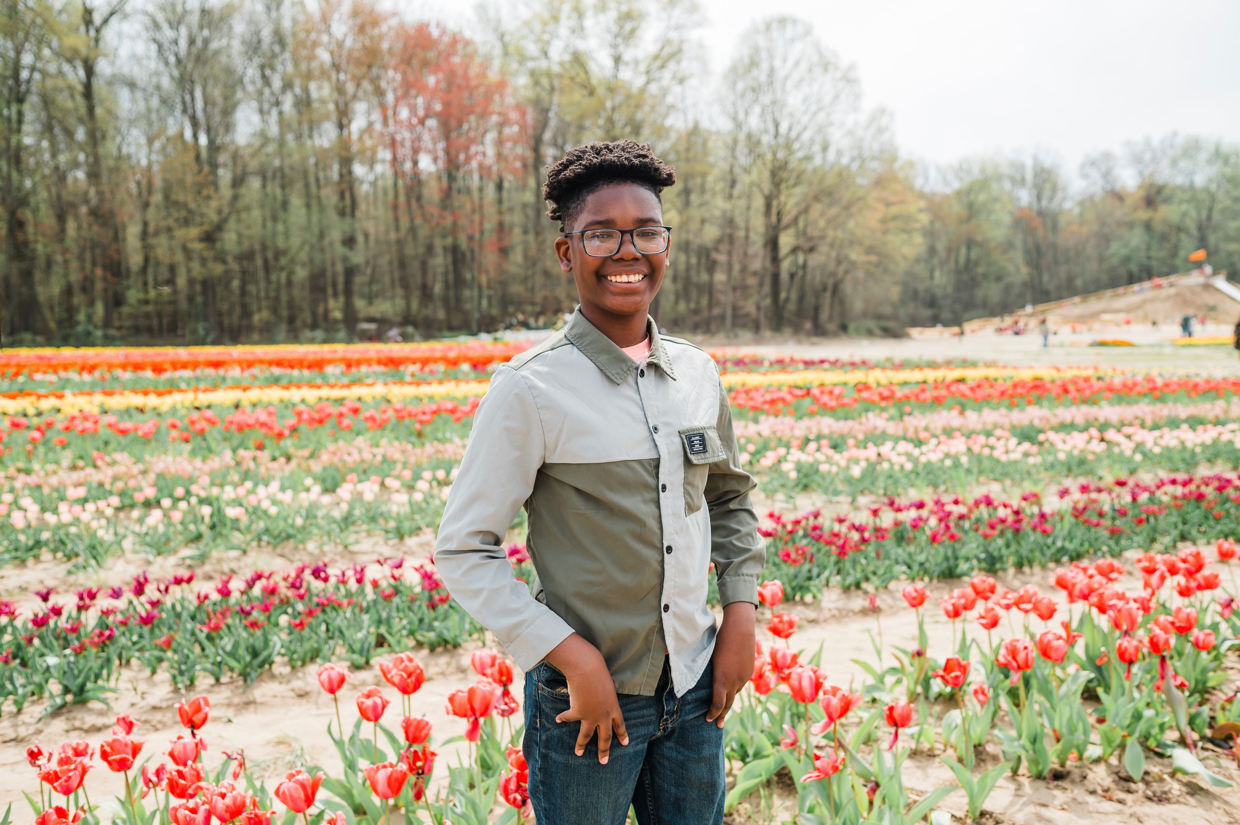 Scenic portrait in a vibrant tulip field with colorful blooms and autumn trees in the background.