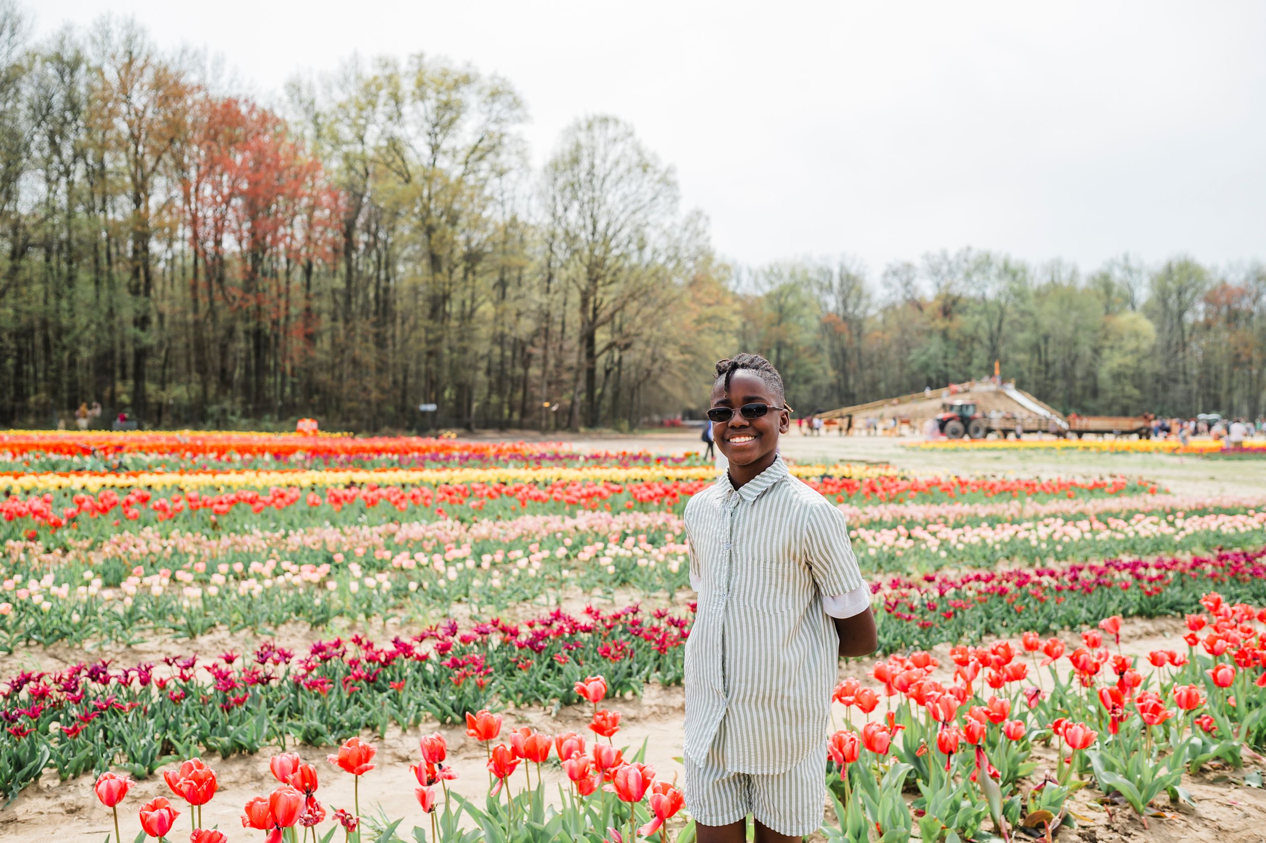 A visitor stands among vibrant rows of colorful tulips at a flower farm on a spring day.