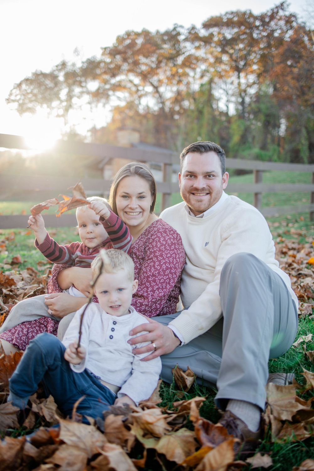 A family lounges together on autumn leaves during a sunset photo session in a park.