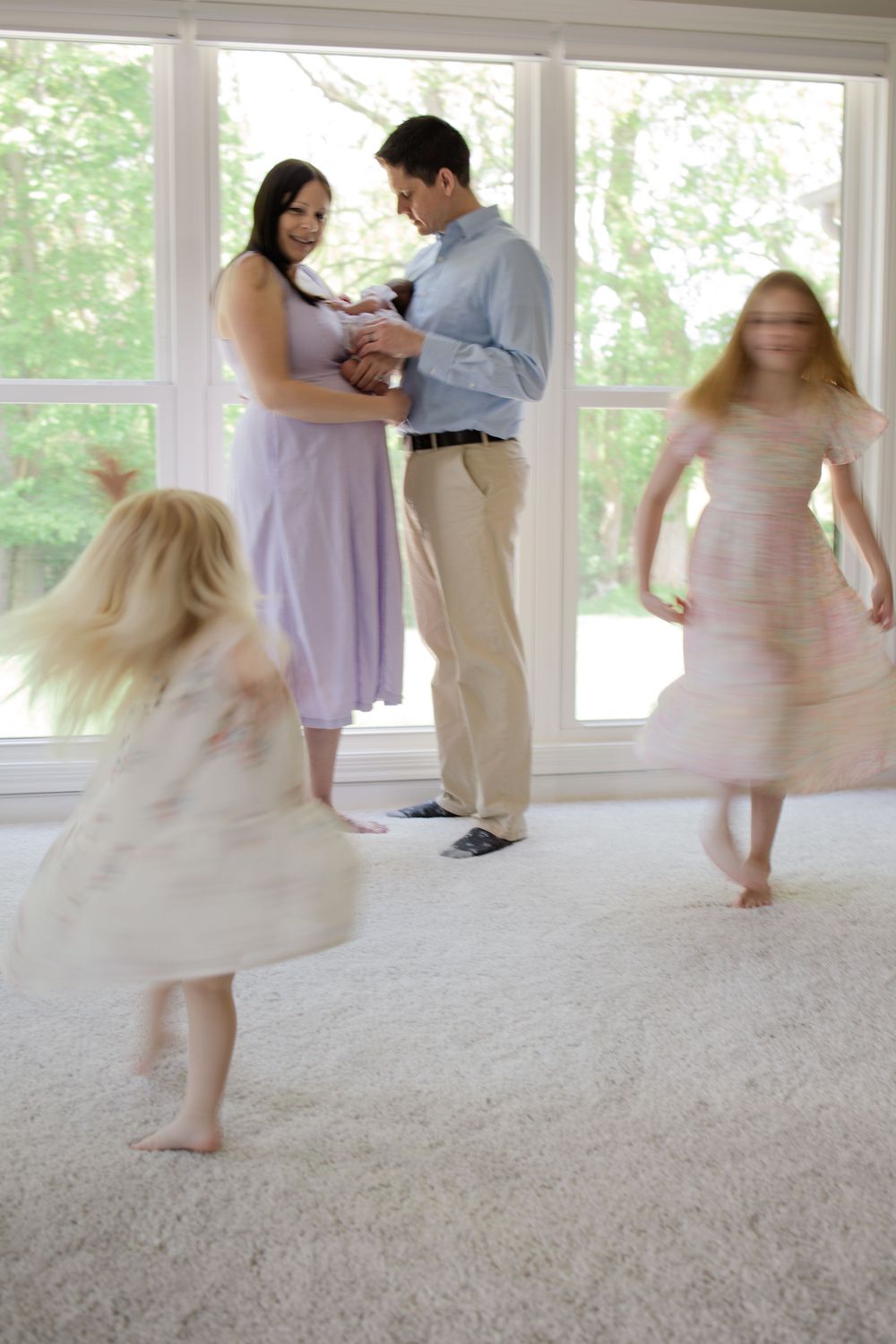 A couple in formal attire dancing with two children twirling in light dresses against sunlit windows.