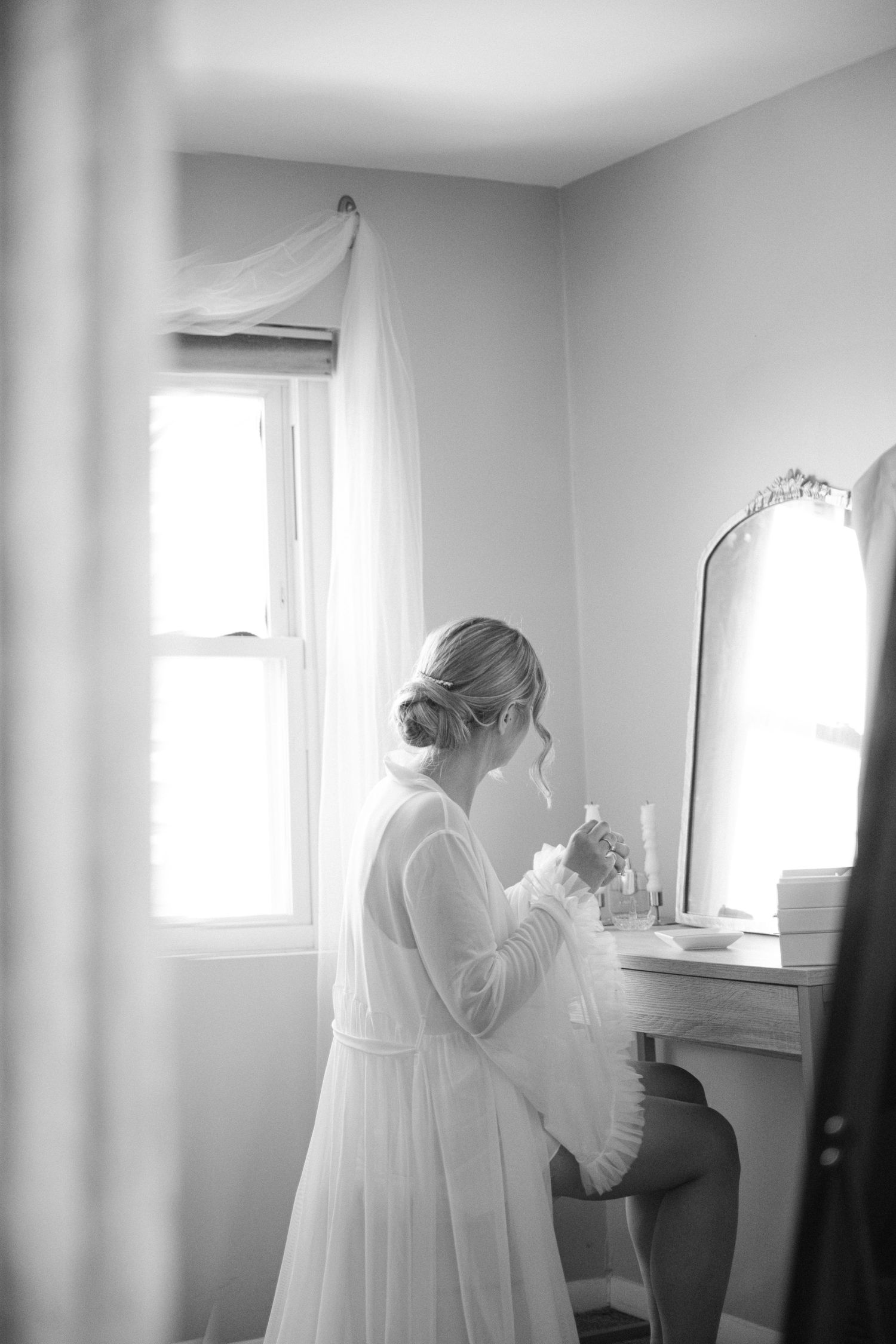 A sequence of black and white photos showing wedding preparation details in a bright room with white curtains.