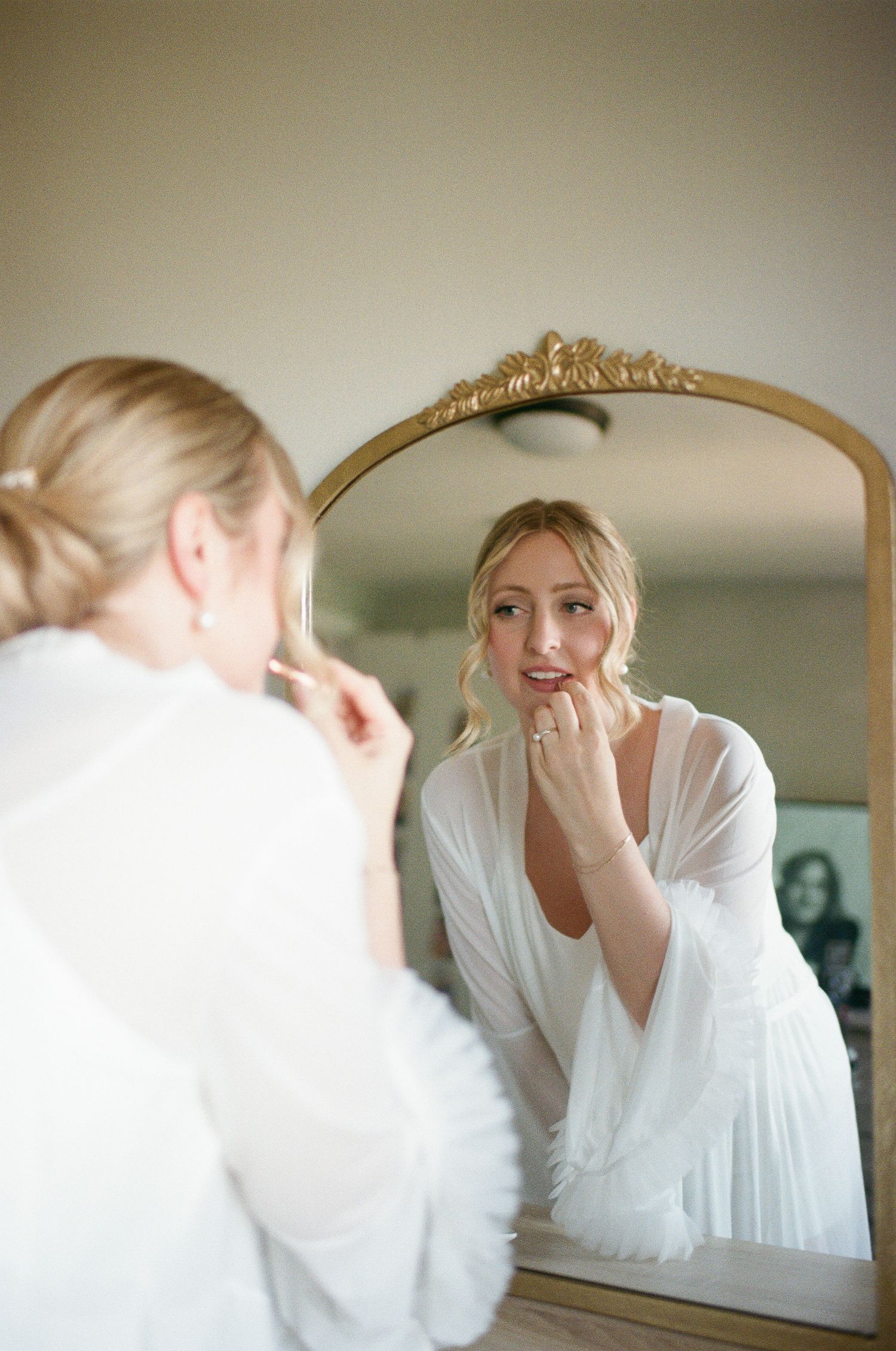 A person in white preparing in front of a mirror with delicate lighting.