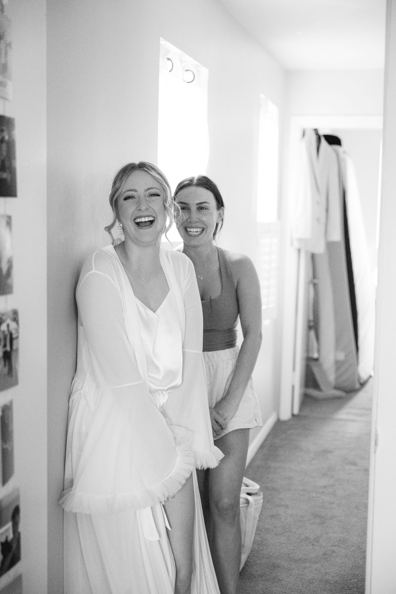 Wedding party sharing joyful moments in bright white hallway.