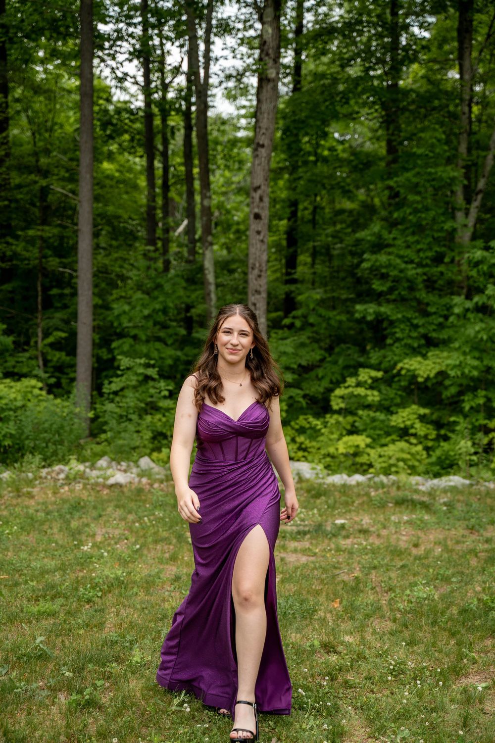 A long purple evening gown with a side slit is worn in a lush forest setting on a summer day.