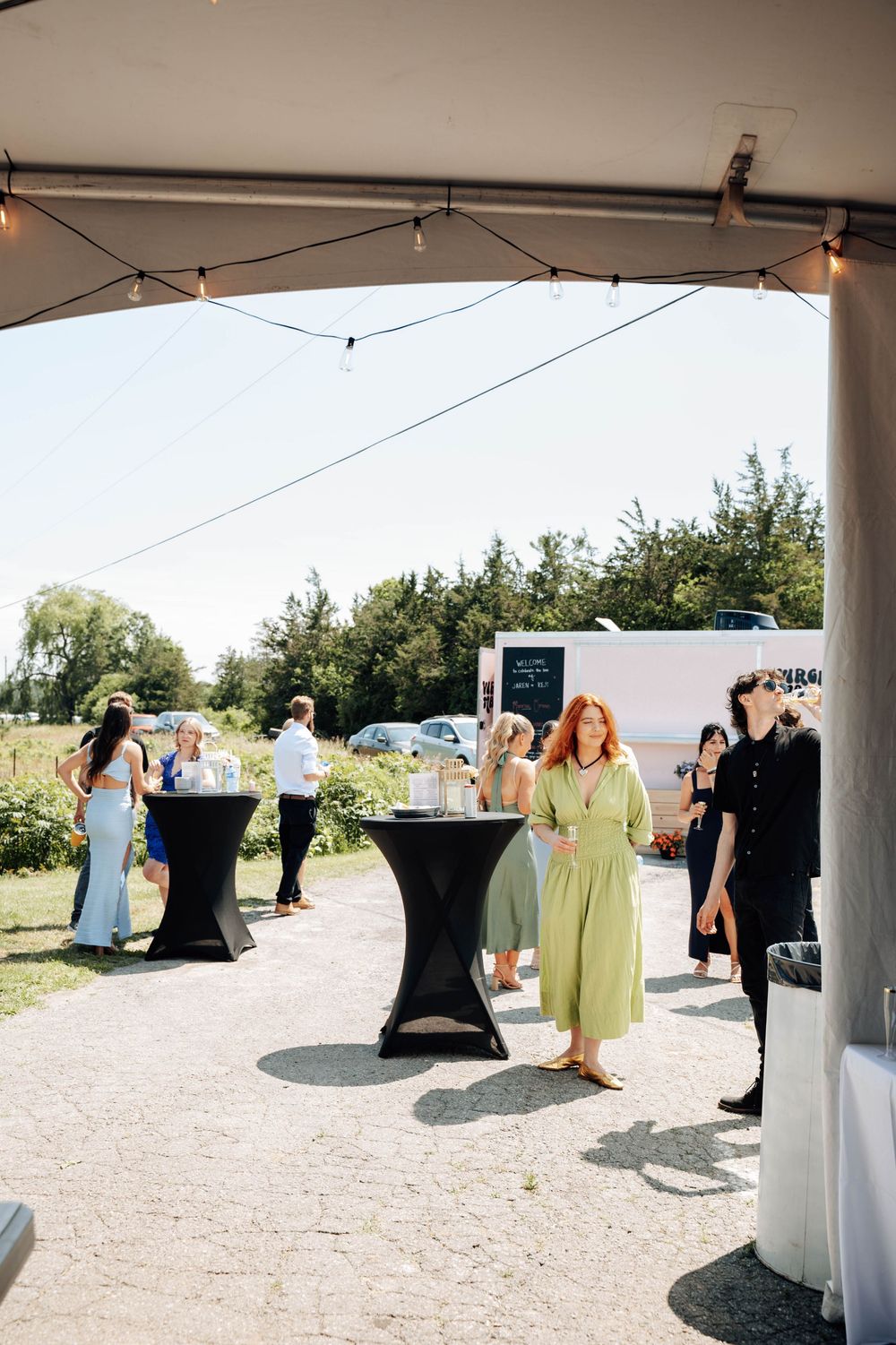 Outdoor reception area with black cocktail tables and tent coverings set up for a wedding event.